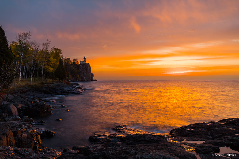 The sun begins to break through a bank of clouds and casts a golden glow on Split Rock Lighthouse perched along the rocky coast of Lake Superior in northern Minnesota.